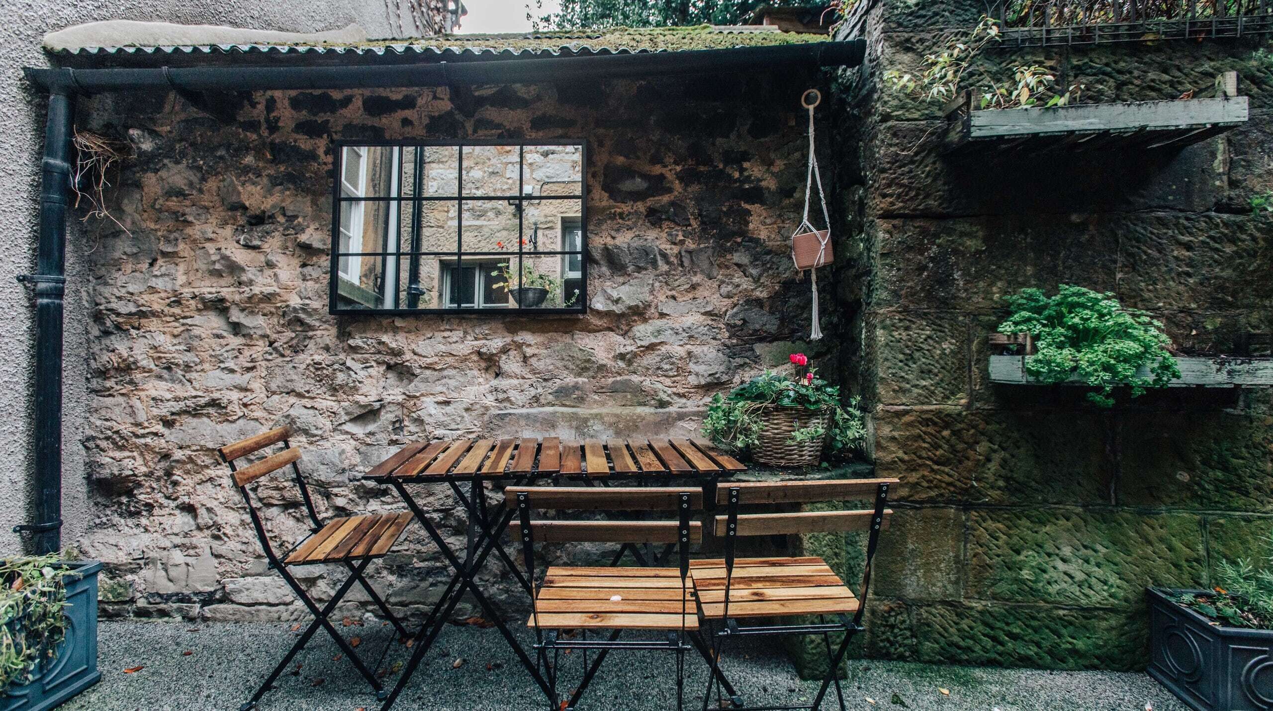 A rustic outdoor seating area with a stone wall, a window, and potted plants.