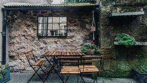 Un área de estar al aire libre de estilo rústico, con pared de piedra, una ventana y plantas en macetas.