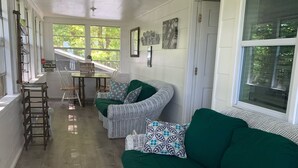 A spacious room with white wicker furniture, a wooden floor, and large windows offering a view of greenery outside. - Maes Cottage In The Clouds (Blue Ridge)