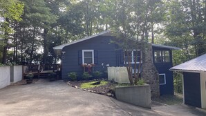 A two-story house with a dark exterior, a front porch, and a small garden area with potted plants and a tree. - Maes Cottage In The Clouds (Blue Ridge)