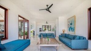 Ein geräumiges Wohnzimmer mit einem großen, blauen Sofa, einem Couchtisch und einem Deckenventilator.