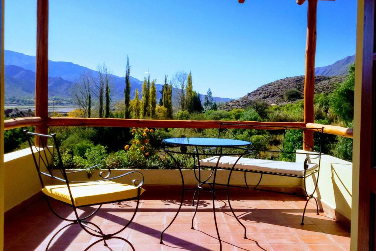 A balcony with a table and chairs, offering a view of a mountainous landscape.