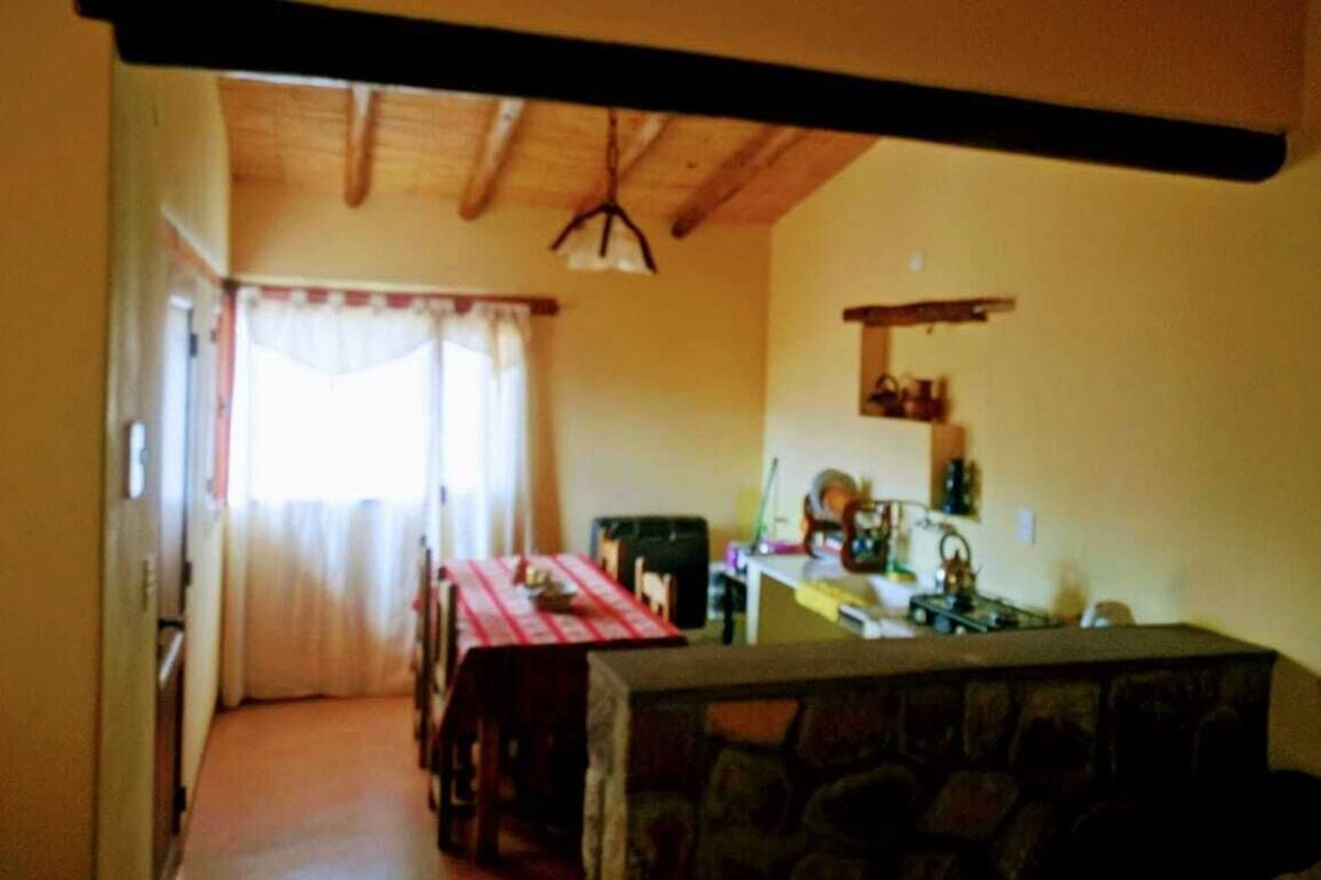 A dining area with a table set for four, a kitchen area with a stove and sink, and a stone bench in the foreground.