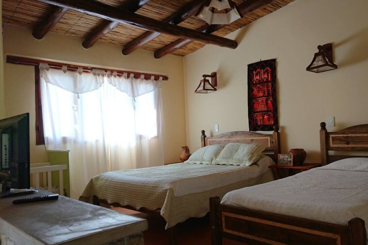 A room with two wooden beds, a small table, a television, and a wall-mounted lamp.