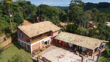 A two-story house with a tiled roof, a stone patio, and a view of the surrounding forest.