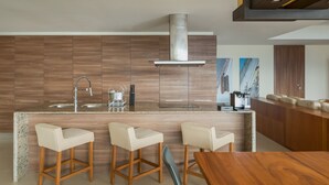 A modern kitchen with wooden cabinetry, a stainless steel range hood, and a bar area with three stools. - Nima Bay Lifestyles Experience (Puerto Vallarta)
