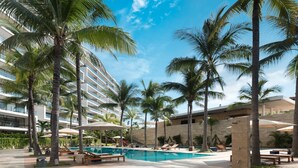 A pool area with palm trees, lounge chairs, and a modern building with balconies. - Nima Bay Lifestyles Experience (Puerto Vallarta)