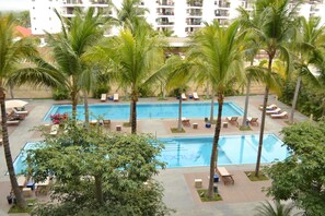 Een resort met twee zwembaden, omringd door palmbomen en ligbedden.