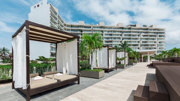 A rooftop lounge area with outdoor seating and a view of a modern hotel building. - Nima Bay Lifestyles Experience (Puerto Vallarta)