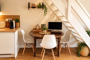 A modern kitchen with a dining area, wooden table, white chairs, and a staircase.