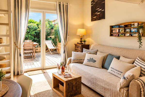 A cozy living room with a sofa, a coffee table, and a view of a garden through a glass door.