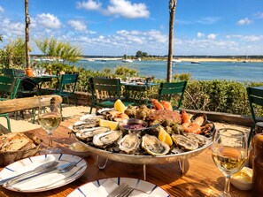 An outdoor dining area with a seafood platter, wine glasses, and a view of the sea.
