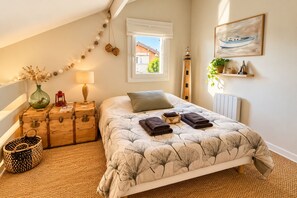 Ein Schlafzimmer mit einem Bett, einem Fenster, einer Heizung, einer Lampe, einer Vase, einem Koffer und einem Korb.