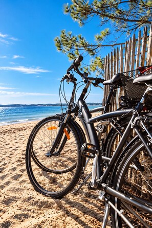 Ein Fahrrad steht auf einem sandigen Strand, im Hintergrund ist ein hölzerner Zaun und ein klarer, blauer Himmel zu sehen.