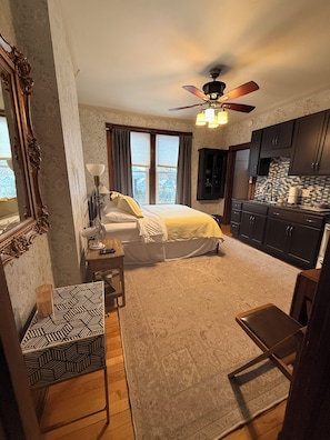 A bedroom with a bed, bedside table, lamp, and a view of the outside.