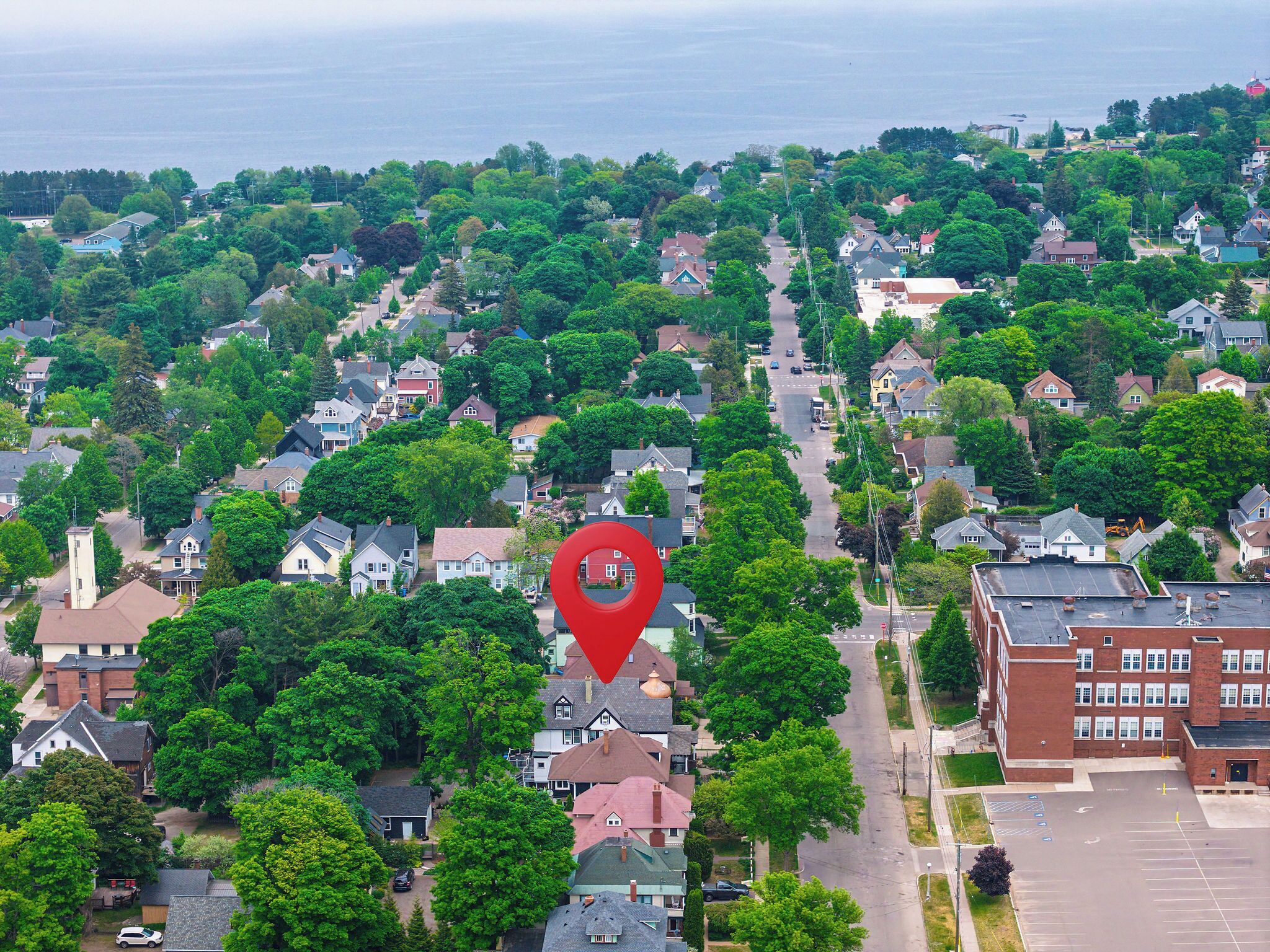 An aerial view of a residential area with houses, trees, and a large red marker indicating a specific location.