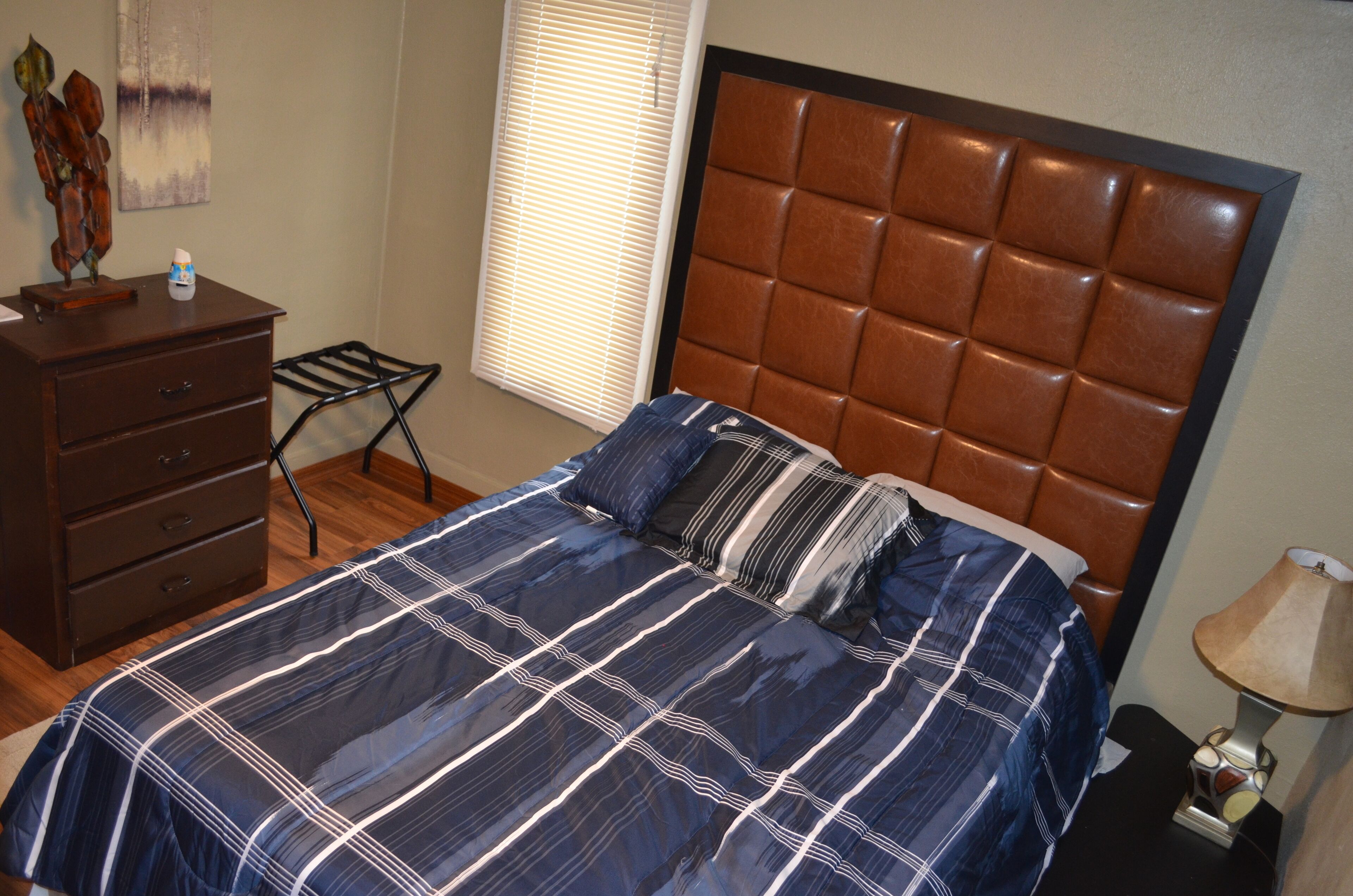 Un dormitorio con cama, cómoda, lámpara y ventana con persianas.