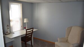 Een kamer met een bureau, stoel, lamp en een raam met jaloezieën.
