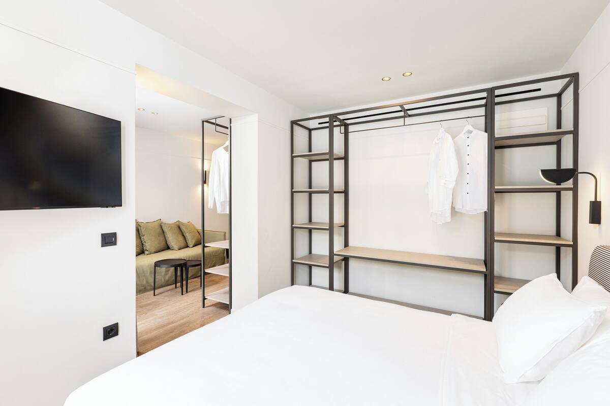 A modern bedroom with a bed, a walk-in closet with shelves, and a TV mounted on the wall.
