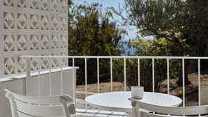 A white outdoor seating area with a table and chairs, a white railing, and a view of greenery and trees.