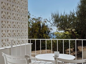 A white outdoor seating area with a table and chairs, a white railing, and a view of greenery and trees.