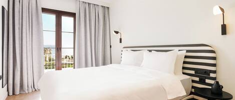 Una habitación de hotel moderna con una cama grande, cortinas grises, un cabecero a rayas negro y blanco, una mesita de noche pequeña y una lámpara de pared.