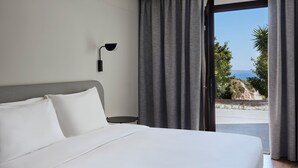 A modern hotel room with a large bed, a nightstand, a wall-mounted lamp, and a view of the ocean through a sliding door.