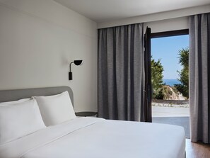 A modern hotel room with a large bed, a nightstand, a wall-mounted lamp, and a view of the ocean through a sliding door.
