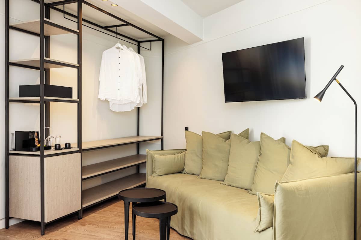 A modern living room with a sofa, a TV, a coffee table, and a shelving unit with a hanging garment.