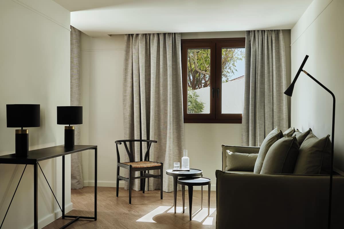 A modern living room with a sofa, two chairs, a small table, and a desk with lamps.