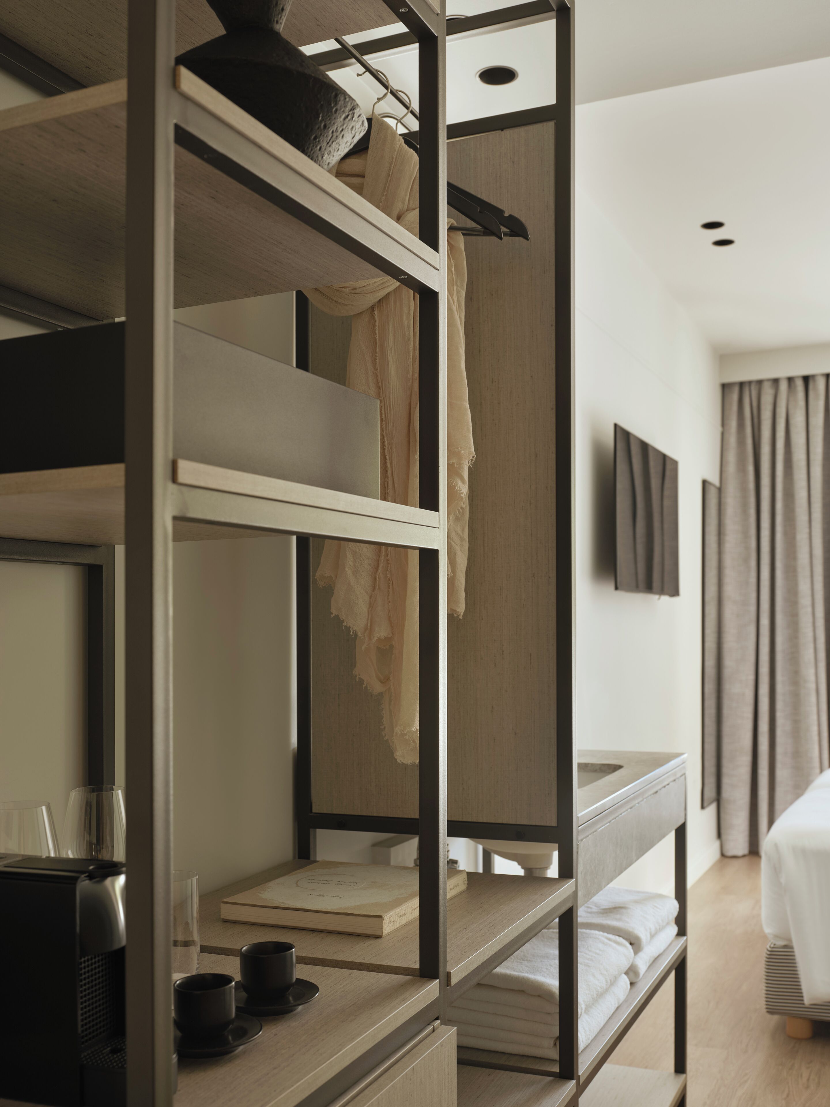 Una cama litera con escritorio y cafetera, un televisor en la pared y una ventana con cortinas.