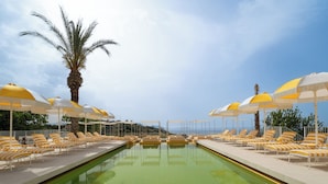A pool area with lounge chairs and umbrellas, a palm tree, and a clear sky. - Doryssa Lithos Hotel (Samos)
