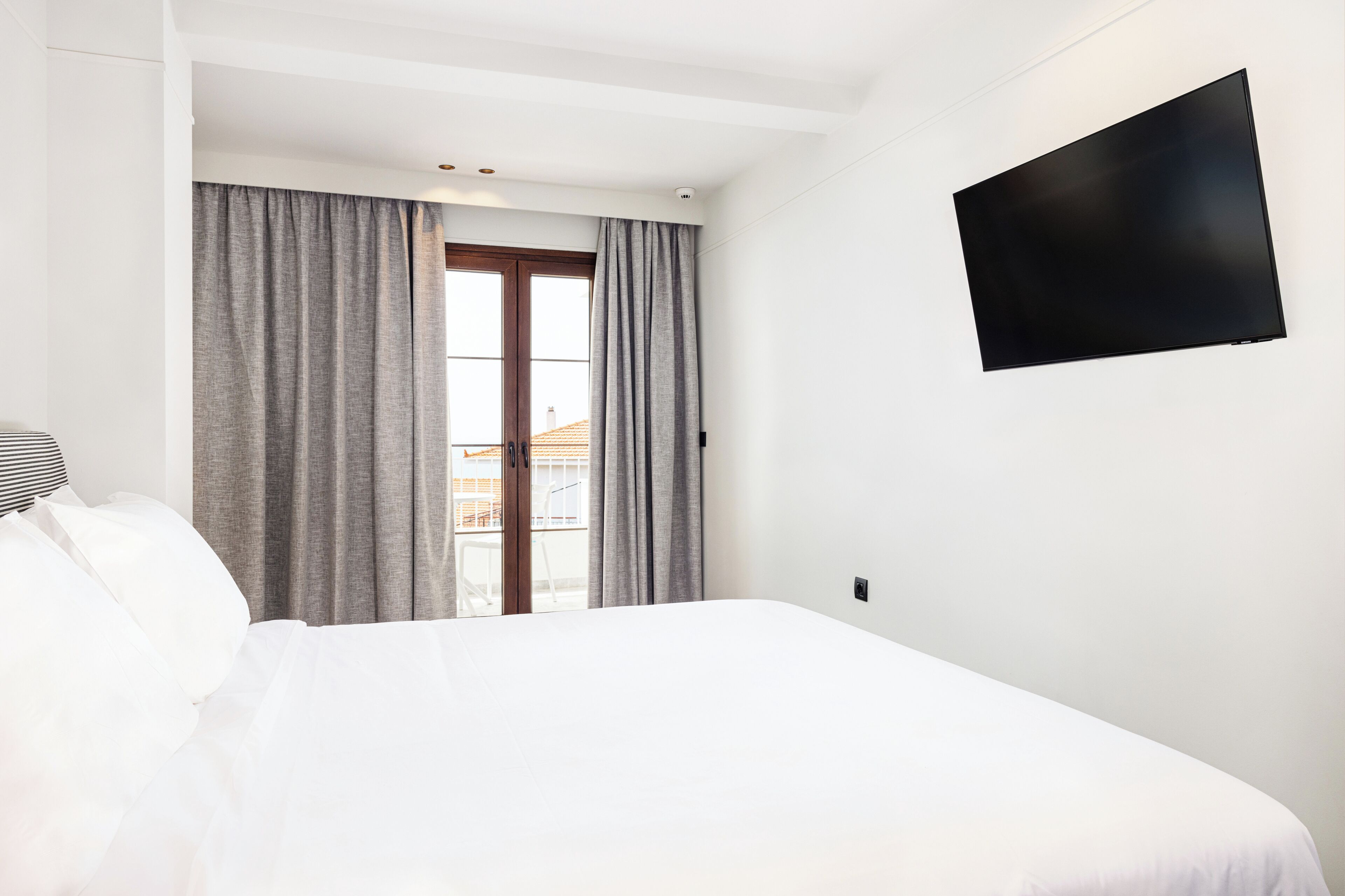 Une chambre d’hôtel avec un grand lit, un téléviseur à écran plat fixé au mur et une fenêtre avec des rideaux.