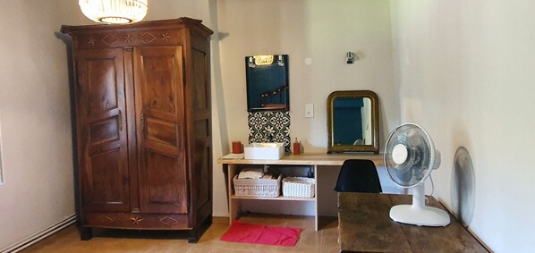 Una habitación con un armario de madera, un espejo, un lavabo blanco, un ventilador y una alfombra roja.
