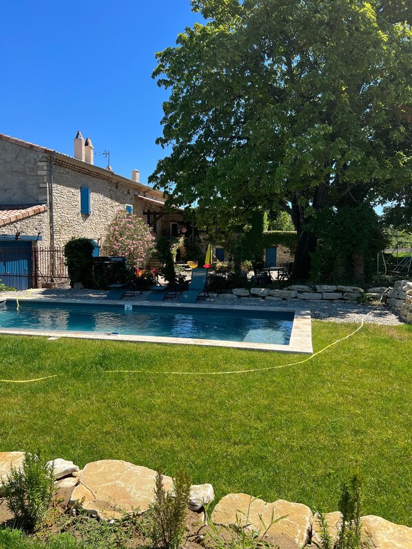 Un bâtiment en pierre doté d’une piscine, entouré d’une pelouse bien entretenue et de gros rochers.