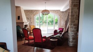 A spacious living room with a stone fireplace, red chairs, and a large window offering a view of greenery. - A charming mas in Drôme provençale, a true family home (Puygiron)
