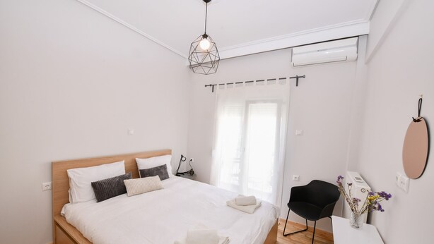 A modern bedroom with a bed, bedside table, chair, and a hanging light fixture.