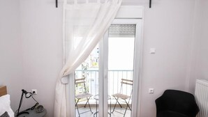 A bedroom with a bed, a bedside lamp, a chair, and a view of an outdoor balcony with chairs.