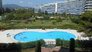 A hotel with a large swimming pool surrounded by greenery and a multi-story building in the background. - Apartment "France II" overlooking Cannes Marina and the Lerins Islands (Mandelieu-la-Napoule)