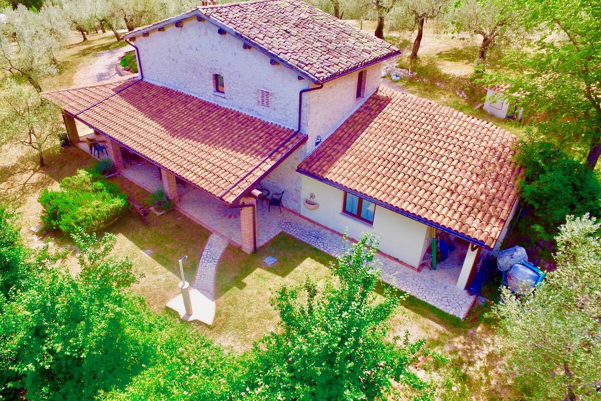 A two-story house with a tiled roof, surrounded by trees and a garden.