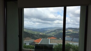 A room with a large sliding glass door leading to a balcony with a view of a hilly landscape and a body of water. - Vald'arêgos Douro Turismo Rural (Resende)