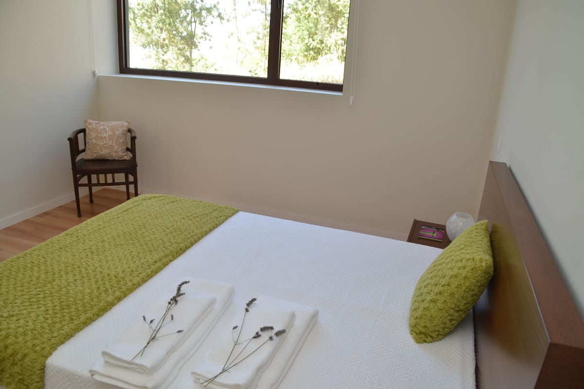 A neatly made bed with a green pillow, a folded white towel, and a decorative branch.