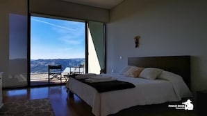 A bedroom with a large bed, a chair, a table, and a view of the mountains. - Vald'arêgos Douro Turismo Rural (Resende)