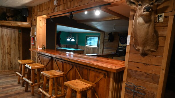 A rustic bar area with wooden stools, a wooden counter, and a mounted animal head. - Bushy Beaver Bar (Big Falls)