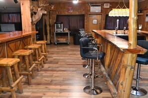 A bar area with wooden stools, a counter, and a deer head mounted on the wall.