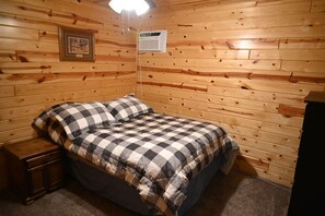 A wooden-paneled room with a bed, a nightstand, a framed picture, and a thermostat on the wall.