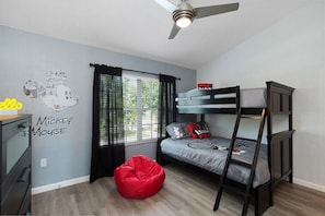 A bedroom with a bunk bed, a desk, a red bean bag, and a Mickey Mouse wall decal.
