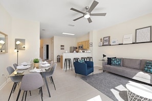 A modern living room with a grey sofa, blue armchair, and a dining area with a table set for four.
