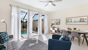 A spacious living room with a large sliding glass door leading to a pool area, a ceiling fan, a dining table set for four, and a TV mounted on the wall. - Charming 3BR Townhome - Private Pool - Walk to Clubhouse - 9 Min Disney! (Kissimmee)