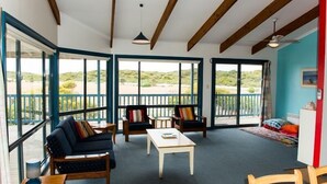 A spacious room with large windows, wooden beams, a sofa, chairs, and a table. - Casadelmar - Prime Position, With Sea Views (Marion Bay)